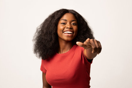 Cheerful Young Woman Pointing at Camera, Inviting Engagement in Bright Studio Settingの写真素材