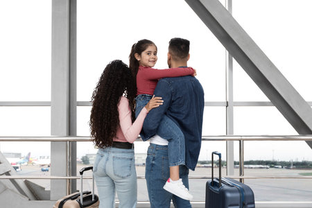 Family Waits at Airport Terminal With Luggage as Child Enjoys Ride on Parents Shouldersの写真素材