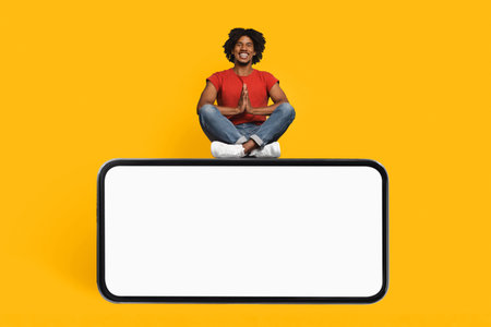 Person in Red Shirt Sitting in Meditation Position on Smartphone Against Bright Yellow Backgroundの写真素材