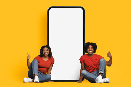 Happy Couple Poses With a Large Blank Screen Against a Bright Yellow Backgroundの写真素材