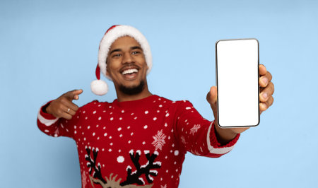 Man in Christmas Sweater and Hat Smiling While Showing Smartphone With Blank Screenの写真素材