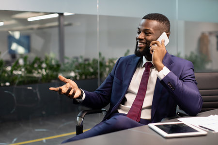 Positive black entrepreneur having phone conversation at officeの写真素材