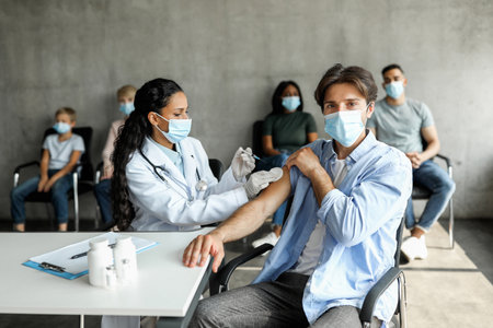 Young man getting intramuscular shot against coronavirus at vaccination siteの写真素材