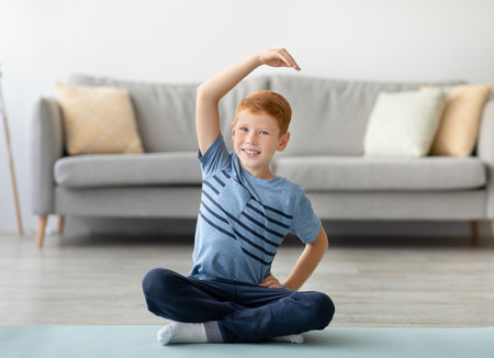 Cheerful Boy Stretching on Yoga Mat in Living Room for Healthy Lifestyleの写真素材
