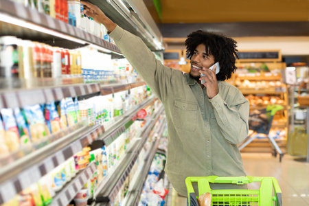 Man Shopping in Grocery Store While Talking on Phone and Reaching for Products on the Shelfの写真素材
