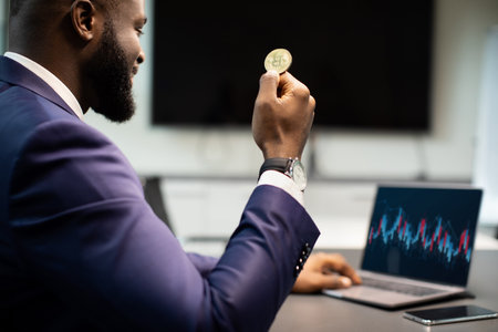 Closeup of african american businessman holding bitcoin, using laptopの写真素材