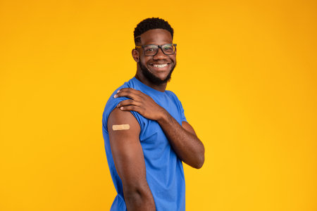Happy Vaccinated Man Showing Arm With Bandage in Bright Yellow Backgroundの写真素材