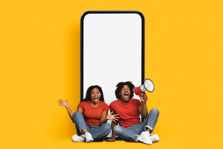 Exciting Couple Celebrating With a Megaphone Next to a Large Smartphone on a Bright Backgroundの写真素材