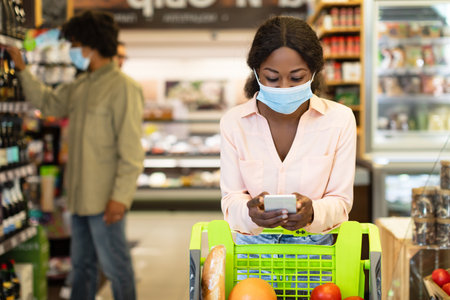Shopping in a Grocery Store During a Pandemic With Individuals Wearing Masks and a Shopping Cart Filled With Groceriesの写真素材