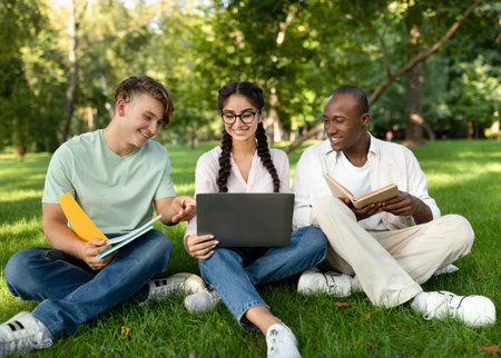 Friends Study Together Outdoors, Enjoying a Sunny Day in the Park While Using a Laptop and Reading Booksの写真素材