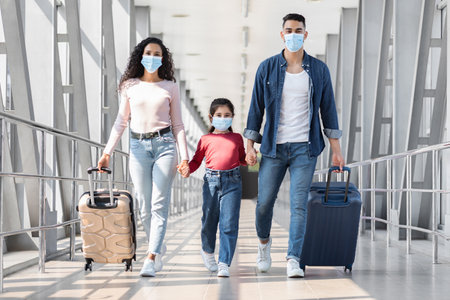 Family With Luggage at an Airport During Travel Wearing Masks for Safety Amidst Health Precautionsの写真素材