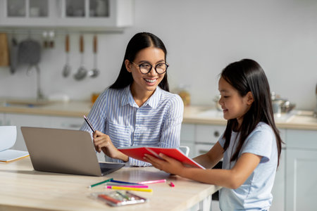 Young Businesswoman Helps Daughter With Homework While Working in Modern Kitchenの写真素材