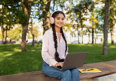 Young Girl Working on Laptop in a Park on a Sunny Day With Headphones Onの写真素材