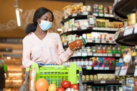 Woman Shopping for Groceries Wearing a Mask in a Store With Green Shopping Cartの写真素材
