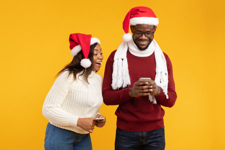 Excited Couple Using Smartphones in Festive Hats While Enjoying New Applications in Studioの写真素材