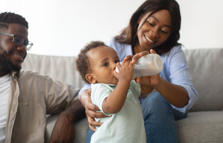 Loving Parents Joyfully Feed Their Toddler on a Cozy Couch in a Nursery Settingの写真素材