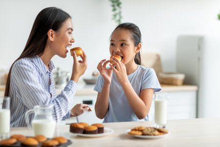 Mother and Daughter Share Delicious Homemade Muffins and Milk in Bright Kitchenの写真素材