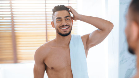 Smiling Man Looking at Himself in the Bathroom Mirror While Drying His Hairの写真素材