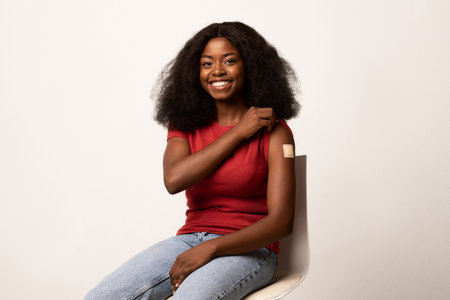 Joyful Black Woman Shows Bandaged Arm Post-Covid Vaccine in a Vaccination Campaignの写真素材