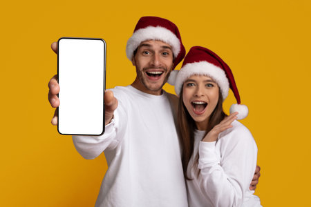 Holiday Celebration With Cheerful Couple Holding Smartphone Against Yellow Backgroundの写真素材