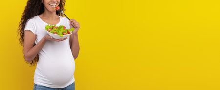 Pregnant Woman Enjoying a Healthy Salad Against a Bright Yellow Backgroundの写真素材