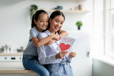 Daughter Surprises Mom With Handmade Gift Card on Mothers Day in a Cozy Kitchen Settingの写真素材