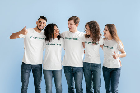 Group of Young Volunteers Smiling Together in Casual Shirts Against Light Blue Backgroundの写真素材