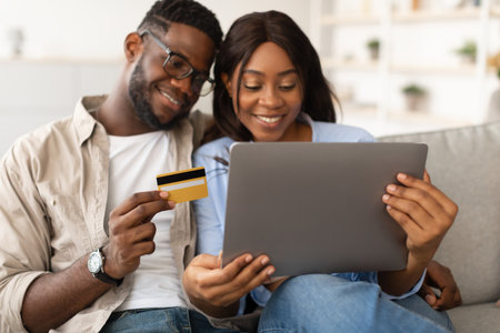 Happy Black Couple Enjoys Online Shopping at Home Using Laptop and Debit Cardの写真素材