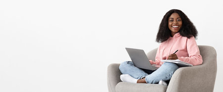Young Woman Studying at Home While Sitting Comfortably in a Cozy Chair With a Laptop and Notebookの写真素材
