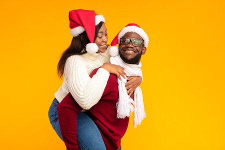 Husband Carries Wife Piggyback in Christmas Spirit Against a Bright Yellow Backgroundの写真素材