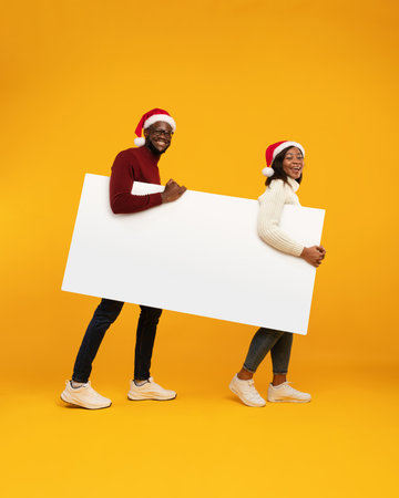 Cheerful African Couple With Empty Poster for Christmas Advertisement on Yellow Backgroundの写真素材
