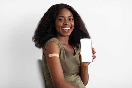 Woman Joyfully Showing Her Phone and Displaying a Vaccination Bandage While Sitting Indoorsの写真素材