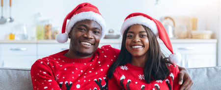 Couple in Festive Sweaters and Santa Hats Enjoying Holiday Moments in Cozy Living Roomの写真素材