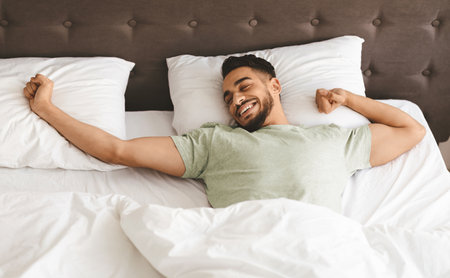 Young Man Enjoying a Relaxing Morning in Bed After a Restful Sleepの写真素材