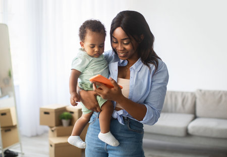 Smiling African American Mom Shows Educational App on Cellphone to Her Young Son at Homeの写真素材