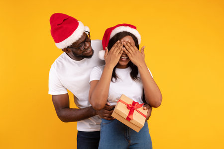 Surprising Girlfriend With a Christmas Gift Against a Cheerful Yellow Backgroundの写真素材