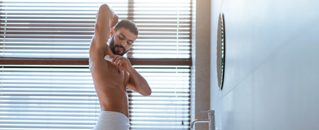 Man Applying Deodorant in a Modern Bathroom in Bright Sunlight During the Morning Hours