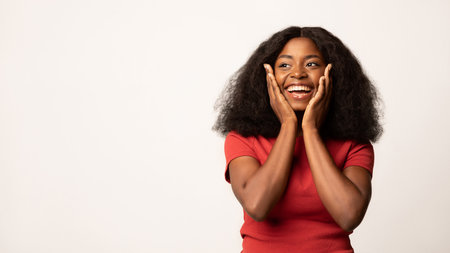 Excited Young Black Woman Touching Her Face and Smiling While Looking Aside With Joyの写真素材