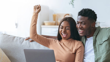 Couple Celebrating a Moment Together While Viewing a Laptop in Their Cozy Living Roomの写真素材