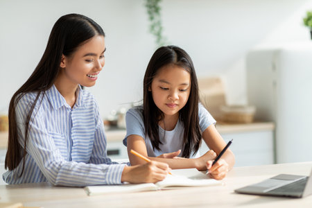 Caring Mother Helps Daughter With Homework in Bright Kitchen During Afternoon Study Timeの写真素材