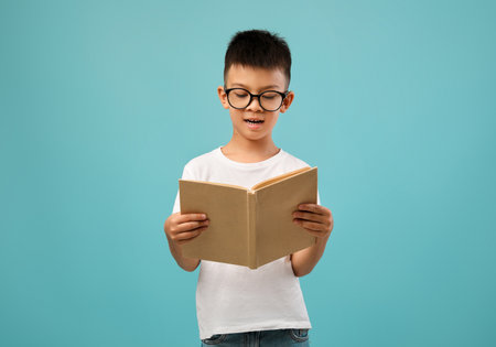 Young Boy Reading a Book With Enthusiasm Against a Blue Backgroundの写真素材