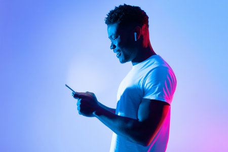 Young Man Using Smartphone With Earbuds in Colorful Lighting at Nightの写真素材