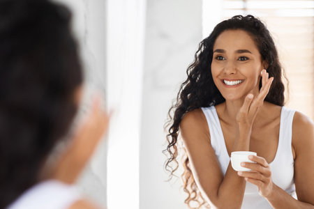 Woman Applying Skincare in Bathroom Mirror With Natural Lighting While Focusing on Her Glowing Skinの写真素材