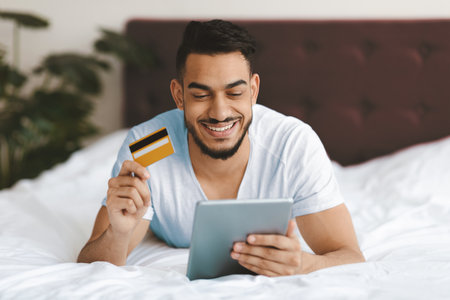 Young Man Enjoys Online Shopping While Lying on Bed in Cozy Room With Plant Decorの写真素材