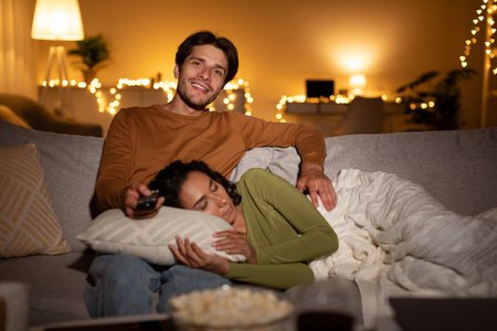 Husband Enjoys Movie Night While Wife Sleeps Peacefully on the Sofa at Homeの写真素材