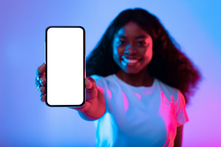 Smiling Woman Showcasing a Smartphone With a Blank Screen in Vibrant Lightingの写真素材