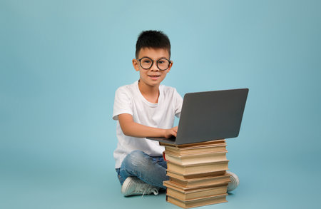 Young Boy Using a Laptop While Sitting on a Stack of Books in a Bright Blue Environment