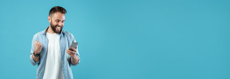 Excited Man Checks Phone, Celebrating Good News in Bright Blue Settingの写真素材