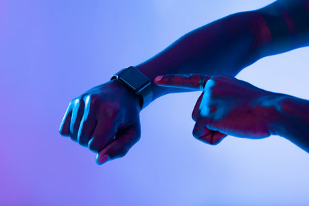 Hand Pointing to Smartwatch With Blue and Purple Lighting in a Modern Settingの写真素材