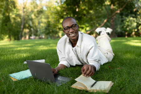 Young Man Studying Outdoors in a Park With Laptop and Notebooks on a Sunny Dayの写真素材